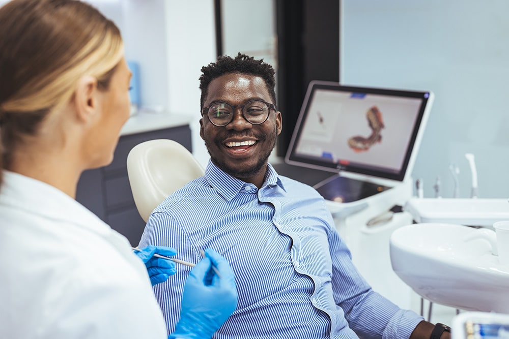 Smiling guy in dentist chair looking with trust at his doctor, talking about tooth extractions.