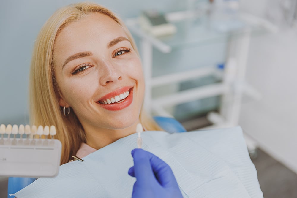 Woman at the dentist choosing veneers enamel color palette with stomatologist compare teeth shade